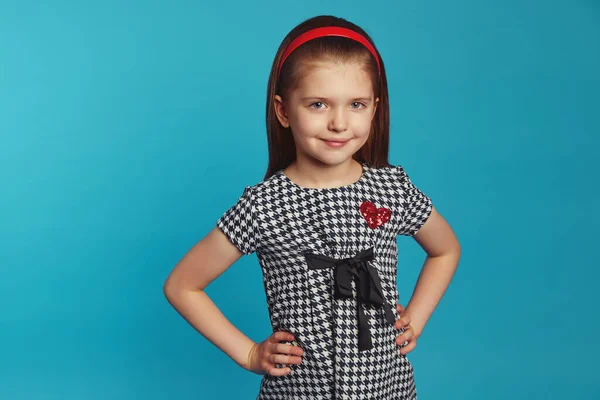 Küçük sevimli kız gülümsüyor ve ellerini mavi duvarın üstünde tutuyor.