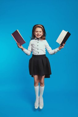Liseli kız mavi arka planda yüksekten atlarken iki defter tutuyor.
