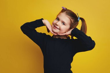 Sarı duvarın üzerinden izole edilmiş kameraya gülümseyen yanaklarla el ele tutuşan kız.