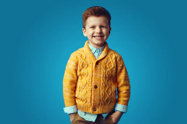 Дитина посміхається, тримаючи руки в кишенях, ізольовані на синьому фоні — стокове фото