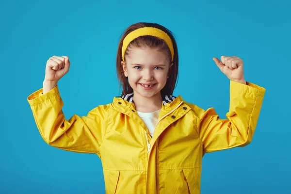Menina levanta as mãos e mostra músculos vestidos com capa de chuva amarela e headband — Fotografia de Stock