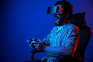 Adam VR gözlükleriyle oyun oynarken yüksek sesle bağırıyor, sandalyede oturuyor.