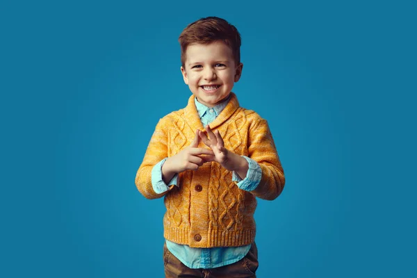 Милий хлопчик у стильному жовтому кардигані посміхається широко на синьому фоні — стокове фото