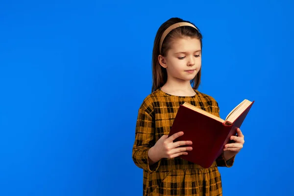 Grave menina leitura livro enquanto pé contra fundo azul — Fotografia de Stock