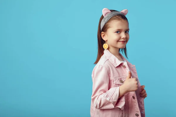 Pembe ceketli kız çok güzel poz veriyor ve mavi başparmağını gösteriyor. 