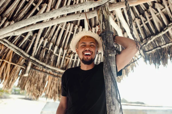 Kumsalda bambu şemsiyenin altında dururken gülümseyen genç turist.