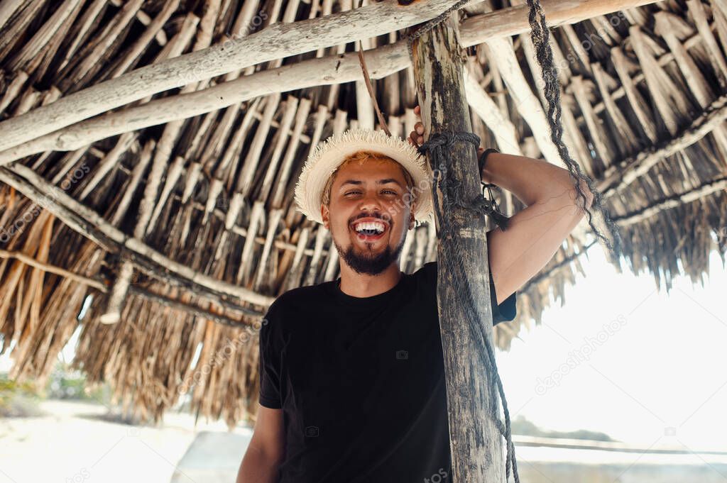 Young tourist man smiling while standing under bamboo umbrella on the beach