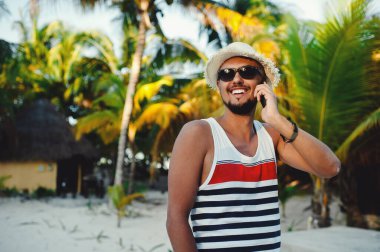 Akıllı telefondan konuşan yakışıklı turist palmiye ağaçlarının arka planında