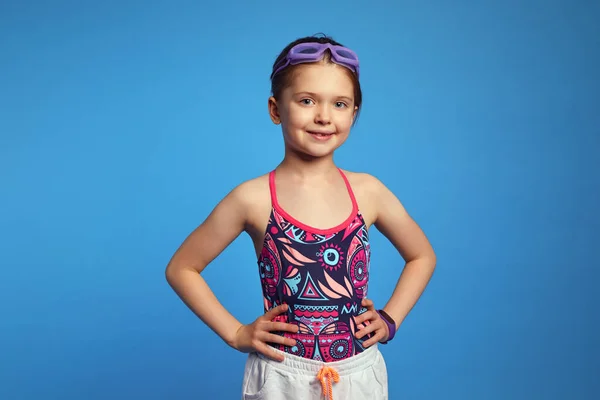 Kendinden emin kız kollarını beline dayayıp yüzmeye hazır gözlükler takıyor ve mayo giyiyor.