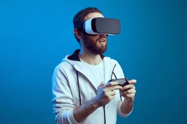 Heyecanlı sakallı genç adam, VR ekipmanlarıyla ayakta duruyor ve oynuyor.