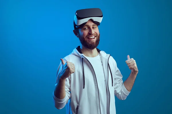 Alnında VR gözlükleri olan adam mavi arkaplan üzerinde başparmak kaldırıyor.