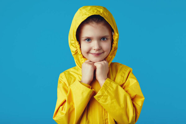 Girl kid wears yellow waterproof raincoat, keeps hands together under chin