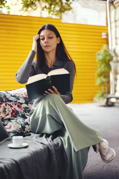 Jovem leitura livro menina enquanto sentado no café com xícara com café quente — Fotografia de Stock