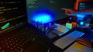 Geliştirici el kodu ekran çalışma alanı ışıklandırması. İnsan eli aydınlanmış monitörü HTML ve Python kodu ile işaret ediyor, klavyeli modern teknoloji kurulumu, notlar, ortam RGB parıltısı, yaratıcı programlama ortamı