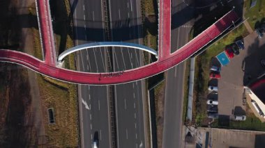 Şehrin banliyöleri üzerindeki yaya bisikleti köprüsü. Poznan yakınlarındaki otoyola yayılan kırmızı ayak ve bisiklet yolunu gösteren hava fotoğrafı yerleşim bölgelerini birbirine bağlıyor şehir ulaşımını ve açık hava aktivitesini teşvik ediyor