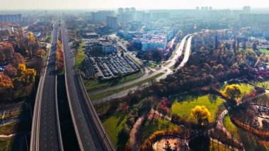Poznan, Polonya, 15 Kasım 2025 Kentsel yeşil alan konut blokları otoyol bağlantısı. Yüksek yoğunluklu konut ve modern yol altyapısı ile harmanlanmış bir şehir parkının hava manzarası güneşli sonbahar günü