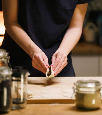 El katlayan mantı hamuru ev yemeği. Kabak mantarı ile mantı şekillendiren tanınmayan kişi, sıcak iç mekan aydınlatması, yavaş yemek hazırlama, aile geleneği havası, Doğu Avrupa yaşam tarzından esinlenilmiş konfor mutfağı sahnesi
