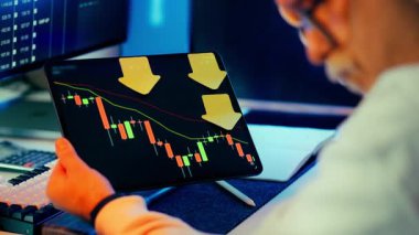 Kripto para birimi analiz tableti modern ofis içi. Kırmızı hamurlu şamdan çizelgesine sahip adam tutma aygıtı sarı aşağı doğru oklar koyu ekran arkaplan çoklu monitör mavi ortam aydınlatma odaklı çalışma alanı atmosferi