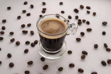 Cam bir fincanda sade kahve ve etrafında kahve çekirdekleri olan bir fincan çay tabağı.