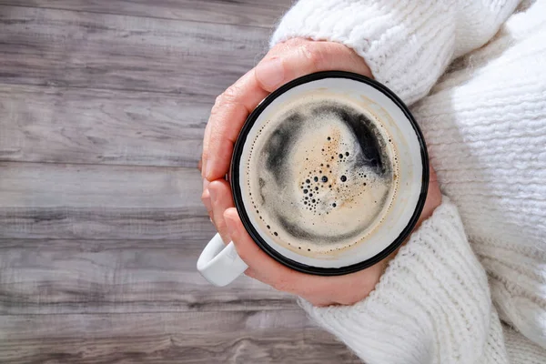 A comforting cup of coffee in the hands of a woman with a big, cosy jumper