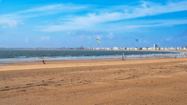 Fransa 'nın Brittany kentindeki Pornichet ve La Baule kasabalarında rüzgar sörfü ve uçurtma sörfü yapan kumsal ve deniz, bölgenin tipik binalarının önünde.