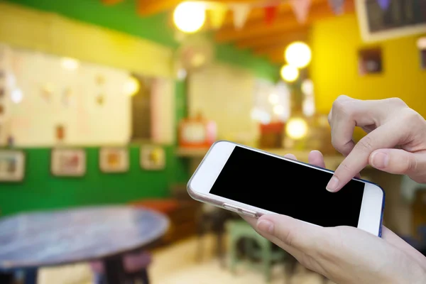 Mujer usando la pantalla táctil del teléfono móvil con la tienda de café borroso atrás — Foto de Stock