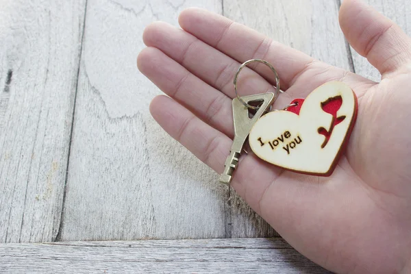 Sleutel van liefde in de hand, hart sleutelhanger op houten tafel — Stockfoto