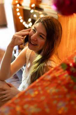 Genç bir kadın mutlu bir şekilde cep telefonuyla iletişim kuruyor, neşeli bir şekilde gülümsüyor gerçek bir festival sezonunda. Tatil kavramı