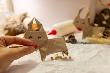 Origami rengeyiği süsleyen bir kadın. Arka planda Noel süslemeleri ve el sanatları malzemeleri yer alıyor. Maddi bakım ve geri dönüşüm kavramı. Ev yapımı süs konsepti