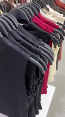 Modern bir giyim mağazasında giysi rafları üzerinde tişörtler. Mevsimsel indirimler ve teklifler kavramı. Üzerinde tişörtler asılı bir elbise rafının yavaş dikey tavası.
