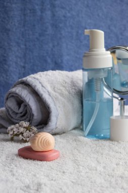 Çeşitli cilt bakım ürünleri, sabun barları, sıvı temizleyicili bir pompa şişesi, rulo havlu ve kurutulmuş çiçekler, sakinleştirici spa deneyimi için yumuşak beyaz bir havluya yerleştirilmiş.