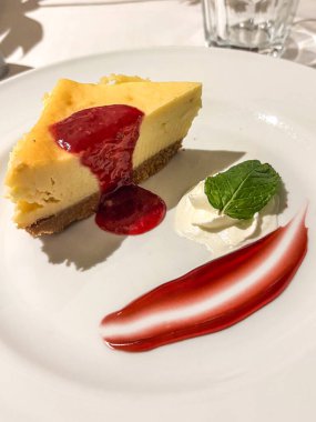 Kırmızı böğürtlen soslu cheesecake sosu, krem şanti, ve beyaz tabakta taze nane şekeri, bir restoranda lezzetli bir gurme tatlısının tadını çıkarmak veya seyahat sırasında