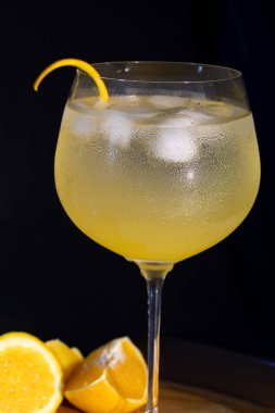 Buzlu cin toniği, portakal kabuğu süslemesi ve ahşap bir zeminde yoğunlaşma, dramatik stüdyo ışıkları yaz ya da gece hayatı için serin, ferahlatıcı ve zarif bir kokteyl sahnesi yaratıyor.