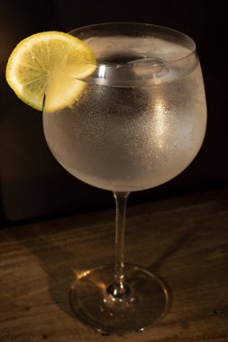 Limon ve buzlu cin toniği. Koyu arka planda. Kırsal bir masa üzerindeki dramatik ışıklandırma altında, soğuk ve zarif bir içecek.