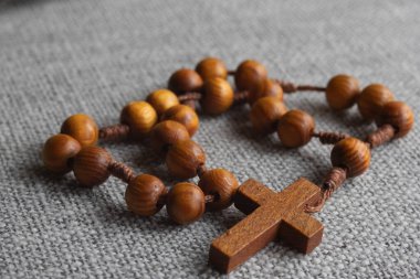 Kalıplı gri arka planda haç takılı basit ahşap tespih, Katolik inancını, duasını, bağlılığını, ruhani yansımasını ve kutsal geleneği simgeliyor.