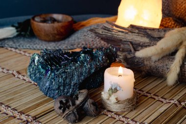 Ruhani sunakta kurumuş çiçeklerle yanan bir mum, büyük yanardöner bir kaya, ahşap elementler ve organik tohum kapsülleri sergileniyor, derin düşüncelere dalmak için sakin bir ortam yaratıyor.