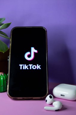 Üzerinde pembe bir masa üzerinde TikTok logosu olan cep telefonu. Mor arkaplanlı. Reklamlar için illüstrasyon kaynağı. Dikey gerçek çekim