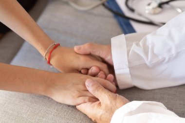 Tıbbi konsültasyon sırasında hastanın elini tutan doktor konfor, empati, güven ve destek öneriyor..