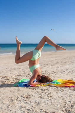Genç kız Tulum, Meksika 'da güneşli bir plajda baş aşağı yoga pozu vererek dengeyi, sağlıklı yaşam tarzını ve yaz tatilini temsil ediyor.