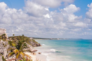 Tulum Maya harabeleri gururla kayalık bir uçurumda duruyor, el değmemiş Karayip plajının ve turkuaz sularının panoramik manzarasını sunarak, çarpıcı bir tarih ve doğal güzellik manzarası yaratıyor.