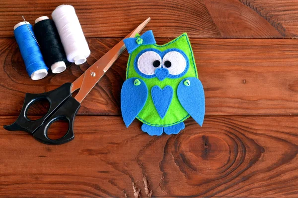 Stitched baby felt owl. Funny bird felt toy, a set of threads, scissors on a wooden table. Crafts sewing felt. Stuffed owl sewing pattern. Fabric owl plush softie. Art and handcraft for kids — стоковое фото