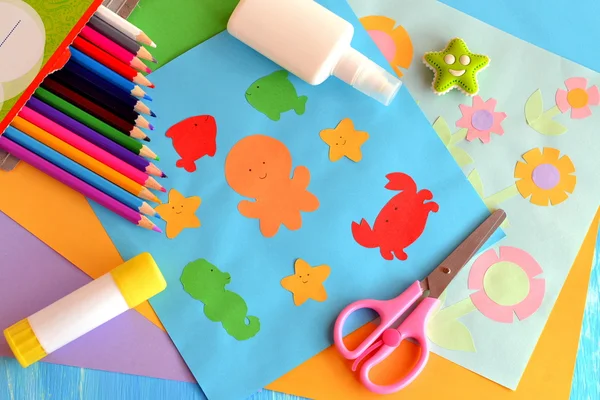 Meerestiere aus Papier und Blumenkarten. Blätter aus farbigem Papier, Scheren, Pensils, Klebstoff kleben auf einem hölzernen Hintergrund. Sommer-Papierbasteln für Kinder zu Hause oder im Kindergarten — Stockfoto