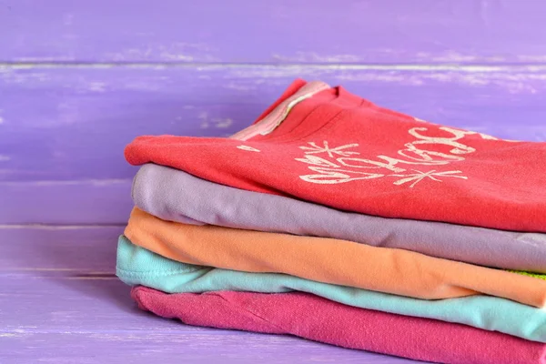 Montón de ropa colorida para las niñas sobre fondo de madera lila. Colección de niñas de algodón raglán. Rojo, lila, naranja, rosa, azul ropa de niños apilados en una pila. Primer plano — Foto de Stock