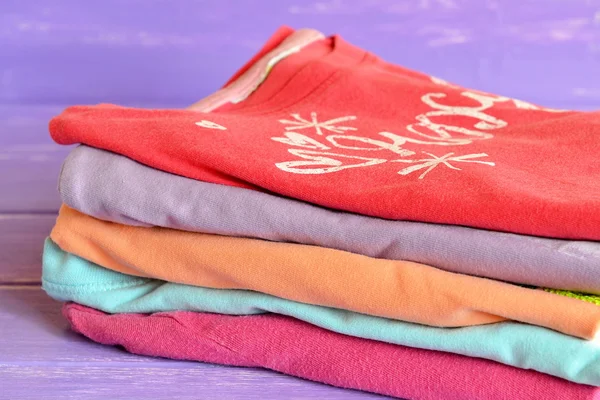 Conjunto de ropa para niños de colores sobre fondo de madera lila. Una pila de elegantes blusas de algodón brillante para niñas. Macro . — Foto de Stock