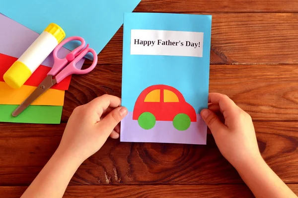 Ребенок держит карточку в руке. Поздравительная открытка с Днем отца. Листы бумаги, ножницы, клей. Как сделать поздравительную открытку на день отца — стоковое фото