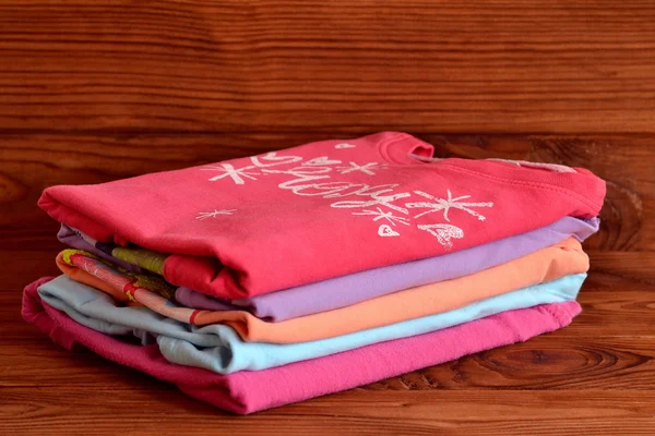 Mezclar tapas de manga larga para las niñas. Montón de ropa colorida de algodón para niños sobre fondo de madera. Cómo almacenar ropa de bebé y niño. — Foto de Stock
