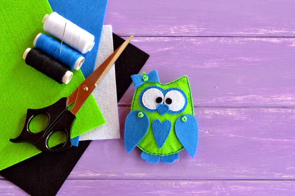 Il giocattolo di gufo è cucito da feltro peluche. Gufo di tessuto verde con cuore e fiocco blu. Idea di arredamento per principianti e bambini. hobby frugale e divertente. Fogli, forbici, filo, ago di feltro colorati — Foto Stock