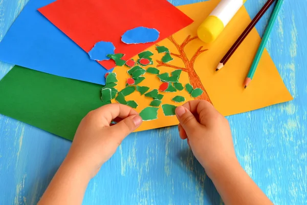 Criança rasgando papel colorido em pedaços. Atividade doméstica para melhorar o desenvolvimento de habilidades motoras finas. Brincadeira de bebé. Como trabalhar com papel e cola. Folhas de papel a cores, bastão de cola, lápis. Fundo azul — Fotografia de Stock