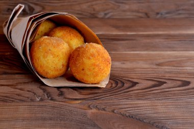 Kahverengi ahşap arka plan üzerinde kağıt arancini topları. Ekmek kırıntıları ve derin kızarmış ile kaplanmış pirinç topları dolması.