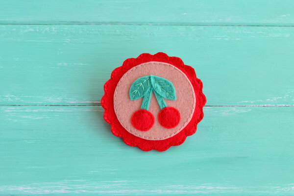 Home felt brooch with berries and leaves. Beautiful handmade wool accessory isolated on a blue wooden background.